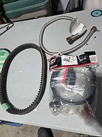 Overview of drive belt, braided hose, and packaged propane hose adapter on table