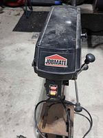 Top view of Jobmate drill press showing brand badge and head unit