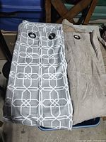 Both curtain panels folded on surface: geometric light grey-blue/white and solid brown