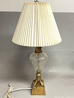 Full view of lamp showing shade, glass body, brass base, and cord