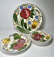 All seven floral plates shown: dinner plate on stand, side plates and stacked saucers