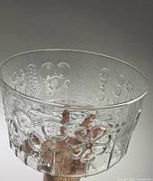 Clear cylindrical glass bowl held in hand showing exterior raised floral pattern