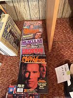Row of bodybuilding magazines featuring Arnold Schwarzenegger and other fitness titles on carpet