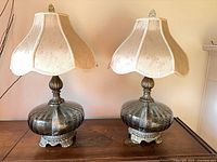 Front view of both lamps on table showing glass bodies, metal bases, and shades