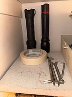 Two black flashlights, masking tape roll, three wrenches on shelf