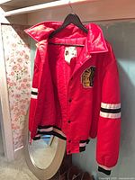 Front view of red Chicago Blackhawks jacket on hanger showing logo and full body