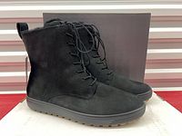 Side view of both boots showing suede uppers, laces, and outsoles with box behind