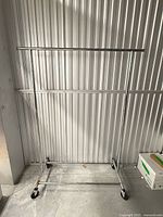 Full view of chrome garment rack standing on concrete floor against corrugated wall