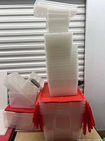Tall stack of small clear bins with lids on top; large red-lid tote at base with more bins beside