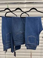 Three pairs of jeans hanging showing overall appearance and back pocket designs