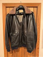 Full front view of jacket on hanger showing leather, collar, pockets, cuffs