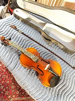 Violin, bow, hard case displayed on padded surface