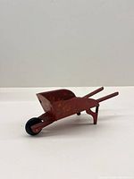 Side profile of antique red wheelbarrow toy showing wheel, legs and handles