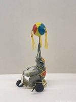 Left view of tin elephant on scooter holding colourful ball