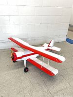 Port front view of red and white RC biplane showing wooden propeller and landing gear