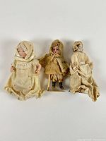 Front view of three bisque dolls showing outfits and size comparison