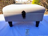 Front view of upholstered ottoman on legs, clasp visible