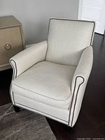 Front angled view of ivory upholstered armchair showing nailhead trim and fabric