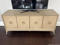 Front view of light tan wood credenza with four doors and brass ring pulls