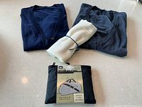 Folded navy and charcoal cardigans, white rolled scarf, REI packable duffel bag