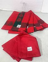 Stack of four plaid pine tree tea towels and four solid red napkins