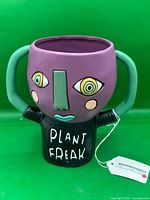 Front view of Allen Designs Plant Freak purple ceramic planter showing face, handles, 'PLANT FREAK' text.