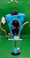 Front view of entire blue teapot clock with teacup pendulum