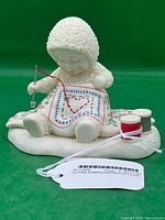 Front view of Snowbabies "Embroidered in Love" figurine with needle, quilt and thread spools