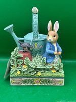 Front view of stone resin figurine showing Peter Rabbit, watering can, bird, foliage, patterned base