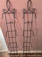 Two identical black iron wall racks leaning against wall