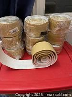 Stack of shrink-wrapped foam baseboard rolls with one roll partially unrolled showing adhesive backing