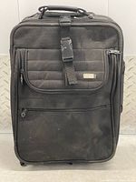 Front view of black fabric carry-on suitcase showing zipper pockets and buckle strap