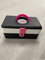 Closed case front view showing pink handle and latch, brand sticker on lid