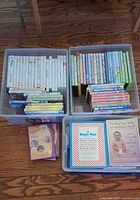 Three clear plastic bins: two filled with children’s DVDs, one with baby books