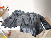 Both black leather jackets laid flat on table