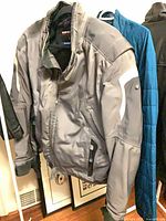 Front of grey BMW Motorrad TourShell jacket on hanger showing reflective trim and zip front