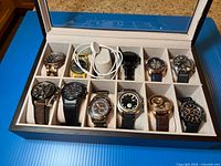Open wood watch box showing one Citizen smartwatch, charging cable and empty slots