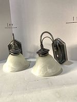 two indoor wall sconces with frosted bell shades on metal backplates