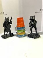 Two black frog musician figurines flanking stacked colored pails