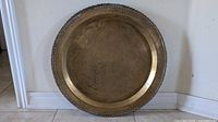 Full view of round brass tray leaning against wall