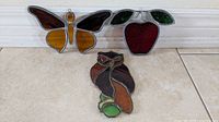 Three stained glass pieces on floor: butterfly, apple, owl