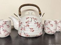 Front view of ceramic teapot flanked by two of the cups