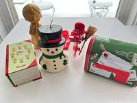 Front view of all main items: wax snowman candle, mailbox tin, book box, gold figurine, clear snowman, red pouch