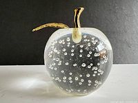 Front view of glass apple paperweight showing bubbles and metal stem/leaf
