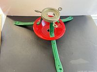 Top view of metal Christmas tree stand displaying green legs, red bowl, galvanized ring