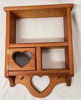 Front view of pine wall shelf showing heart cutouts, mesh door, open shelf sections, and lower pegs