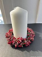 White pillar candle standing inside red and green frosted berry wreath