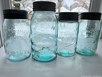 Front view of four aqua glass jars with lids showing logos