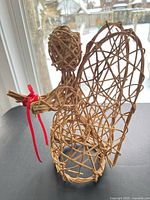 Front left view of wicker rattan angel figurine showing red ribbon and lattice construction