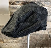 Side profile of dark grey herringbone flat cap on stand